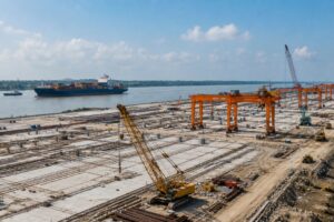 Terminal portuaria en construcción junto a un río con grúas y buque portacontenedores